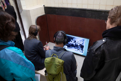 Besucher schauen sich eine künstlerische Videoarbeit am Monitor auf dem Boden an