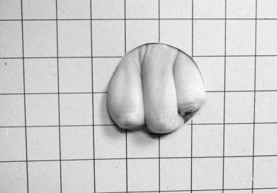 A Hand is pressing itself through a circular opening in a tiled wall.