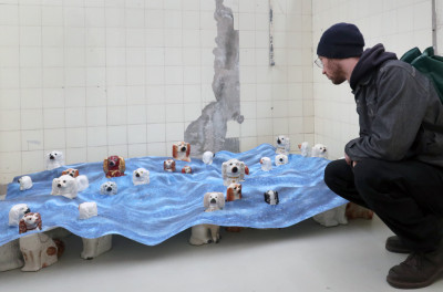Ein Mann betrachtet eine Kunstinstallation mit kleinen weißen und braunen Hundefiguren in der Ausstellung