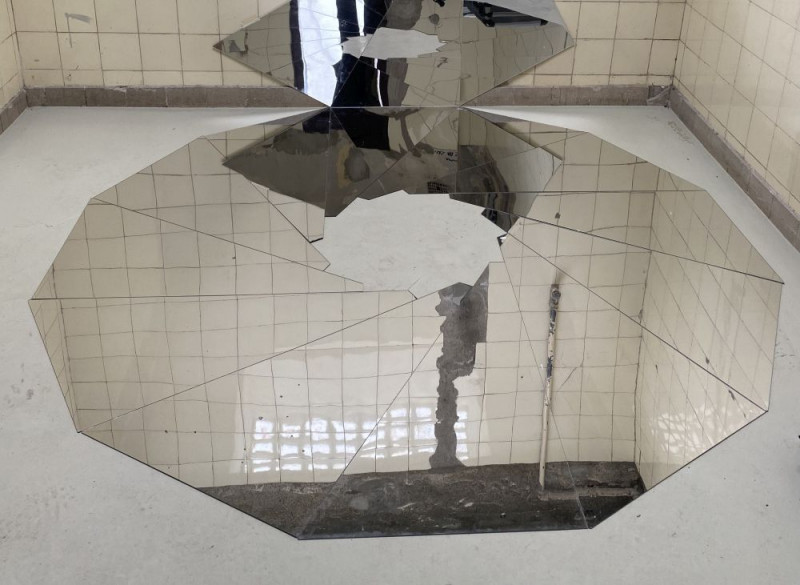 Auf dem Boden der Galerie liegen verschiedenen Spiegel, in denen sich die Fliesen der Wand spiegeln.