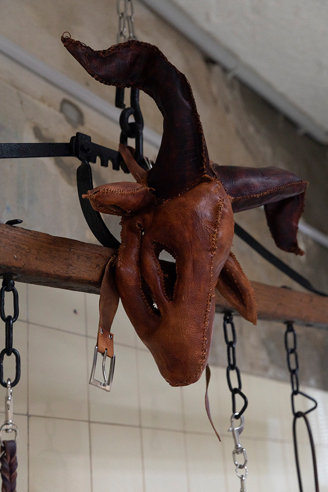 text: 'Lederne Maske einer Ziege in Braun- und Burgundertönen, aufgehängt an einem Holzbalken'
decorative: false
source: reviewed