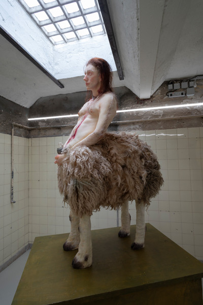 Sculptural artwork depicting a human-sheep hybrid, displayed in an institutional gallery space