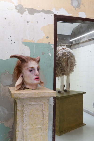 A sculptural installation with a bust featuring exaggerated features on the left and a woolly sheep viewed from behind on the right