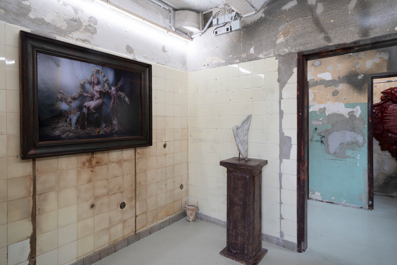 text: >
  Ausstellungsraum mit beschädigten
  Wänden, an der linken Wand eine
  Fotografie in dunklem Rahmen, in der
  Raummitte ein Sockel mit Skulptur und
  offene Türen zu angrenzenden Räumen
decorative: false
source: reviewed