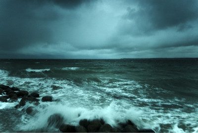 Eine Fotografie der stürmischen Ostsee. Der Himmel ist grau, unten mittig schlägt gerade eine Welle um