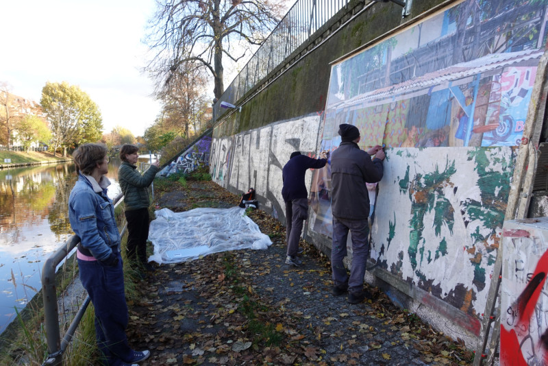 Mehrere Menschen bringen das neue Plakat an der Plakatwand an.