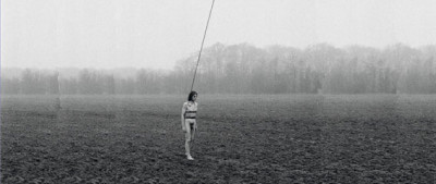 ein nackter Mann läuft über ein Feld und hat einen langen Stab an seinen Körper gebunden