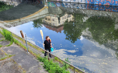 Performance artist Klara Hobza with broom and bucket standing at the Landwehr Canal