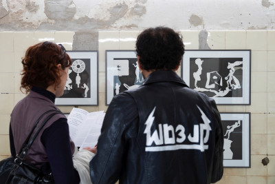 Two visitors are looking at photograms on a wall and studying an information sheet