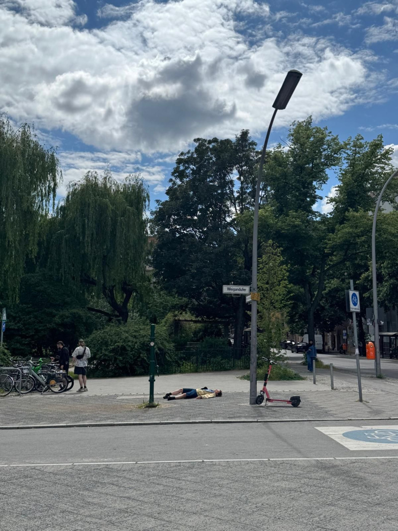 text: >
  Straßenszene mit Künstlerin auf dem
  Boden liegend, Fahrrädern und E-Scooter
  unter bewölktem Himmel
decorative: false
source: reviewed