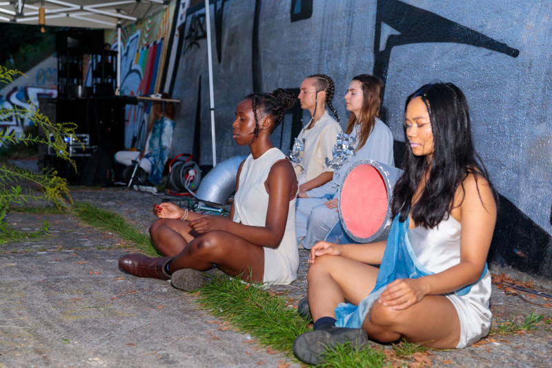 Die Performer*innen meditieren sitzend.