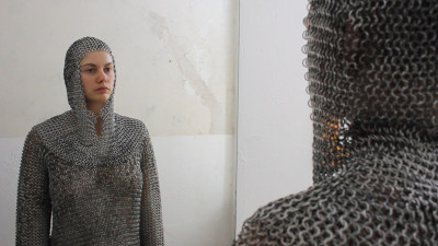 Woman wearing chainmail suit standing against wall
